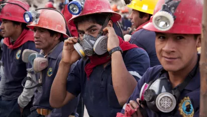 Some men from Peru in red hard hats and face masks are working and looking in the camera