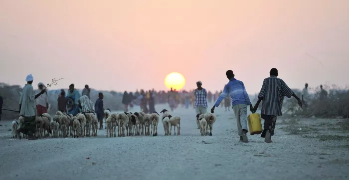 Two young boys carrying water walk down a road next to a camp for internally displaced persons in Somalia.