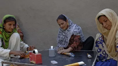 Three women sitting around a table rolling paper.