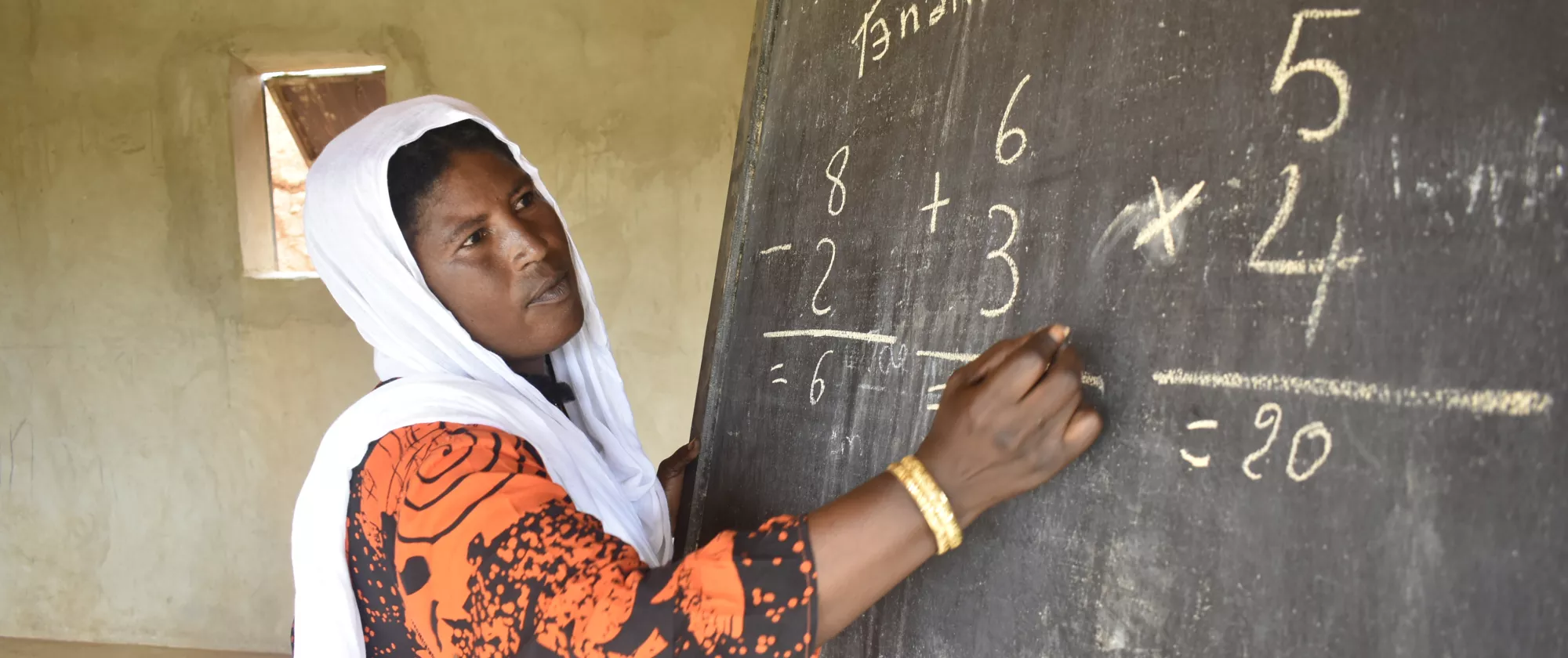 A woman from Niger corrects a maths exercise on a blackboard