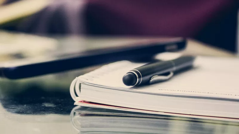 Photo of a notepad with a pen placed on top of it.